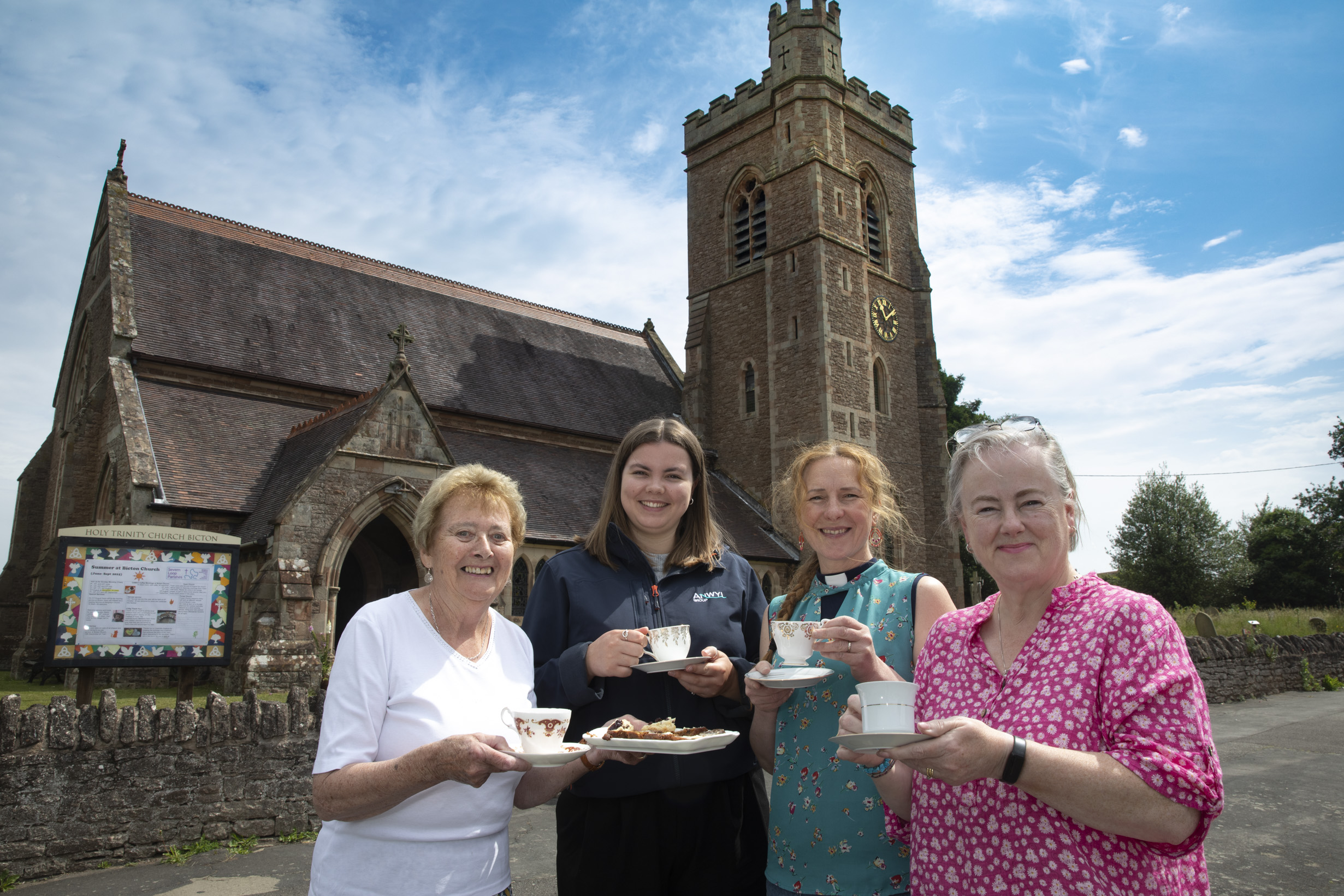 Four women standing in front of church hold tea and cakes